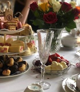 Table laid with a cake- stand containing some petite-four cakes,dish of strawberries & cream and a crystal wine glass.